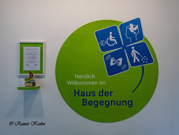 Logo vom Haus der Begegnung mit Ehrenurkunde (Blick aus dem Foyer)